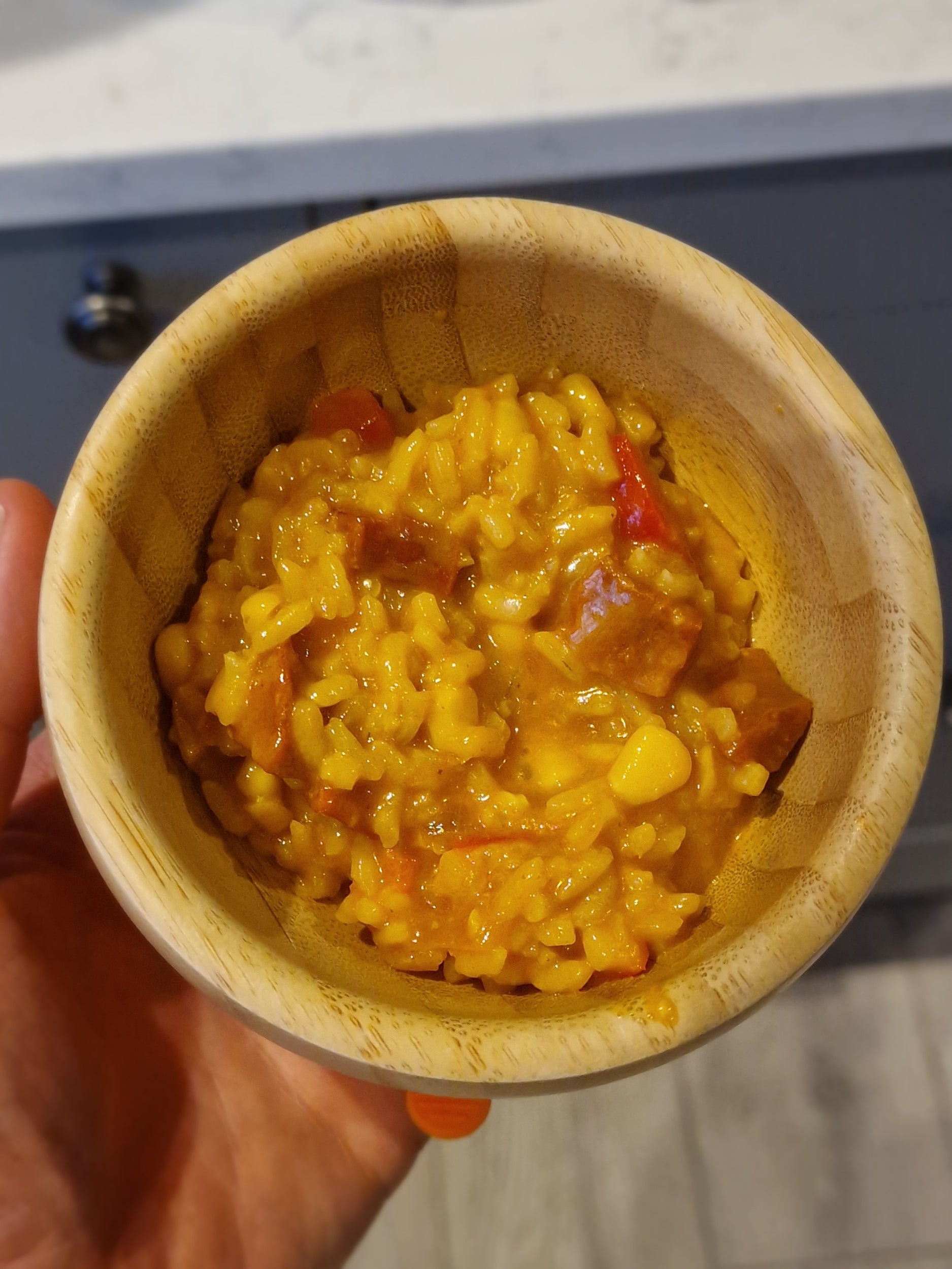 Wooden bowl filled with chicken and chorizo sweetcorn risotto held by a hand against a neutral background